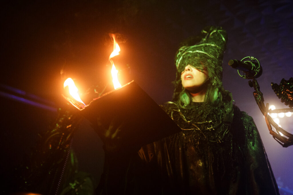 Sick and Beautiful band performing live, the singer is holding a flaming book in her hands.