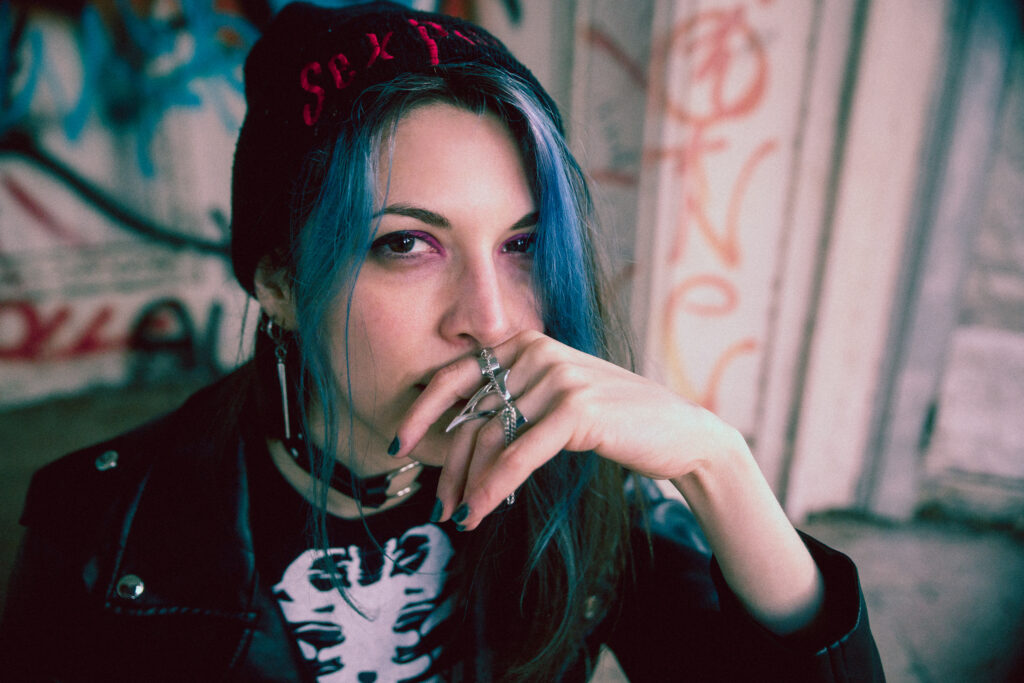 Close up photograph of a punk girl with blue hair inside an abandoned building with graffiti on the walls.