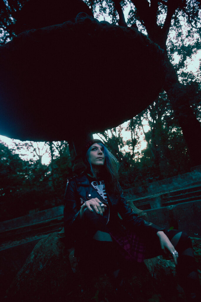 Photograph of a punk girl with blue hair sitting inside an inactive fountain.