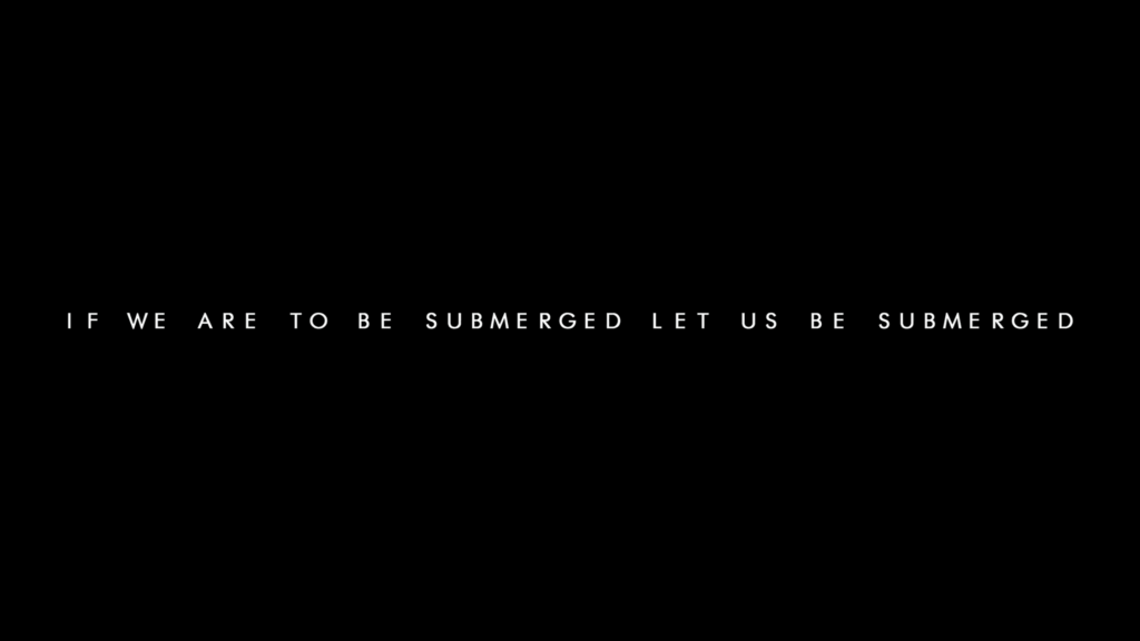 Still from Sleep Token's 'Fall For Me' music video. Black frame with "if we are to be submerged let us be submerged" written.
